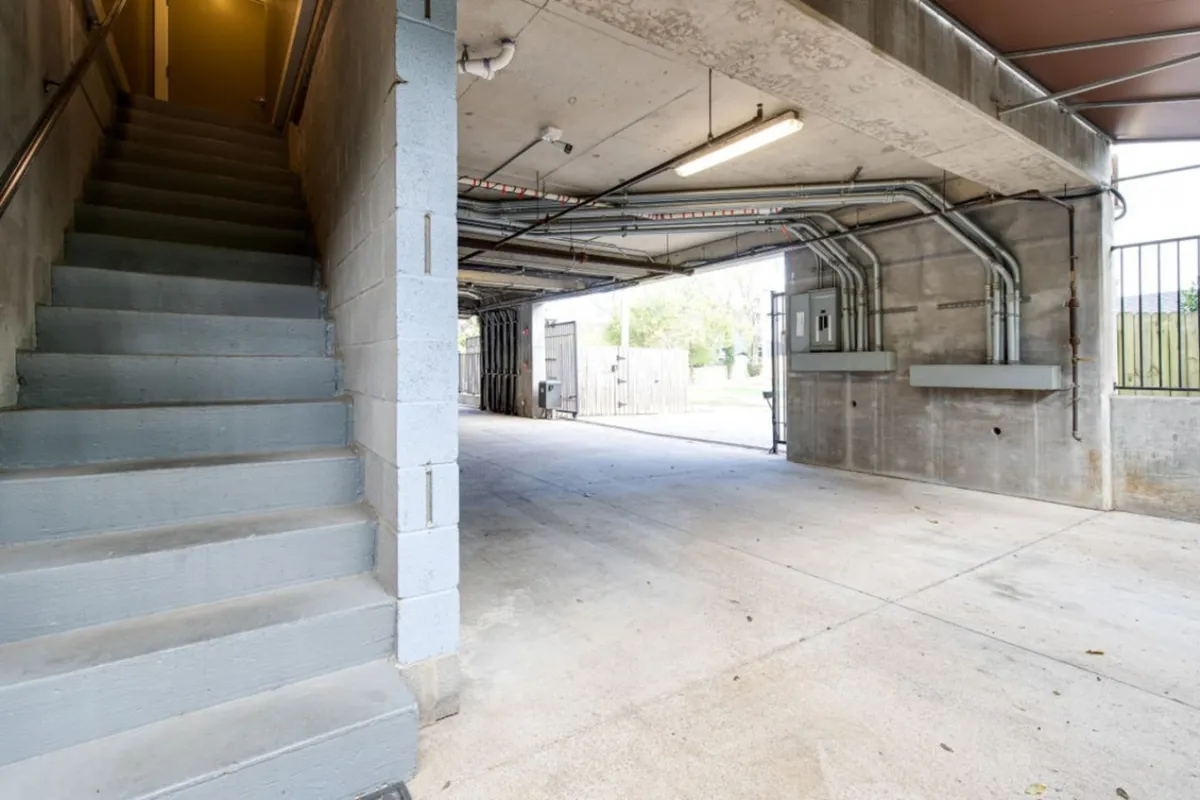 This image shows an open garage space with a visible staircase and exposed pipes, emphasizing the property's practical aspects. The garage is spacious, suitable for multiple vehicles, and highlights ease of access for guests arriving with cars.