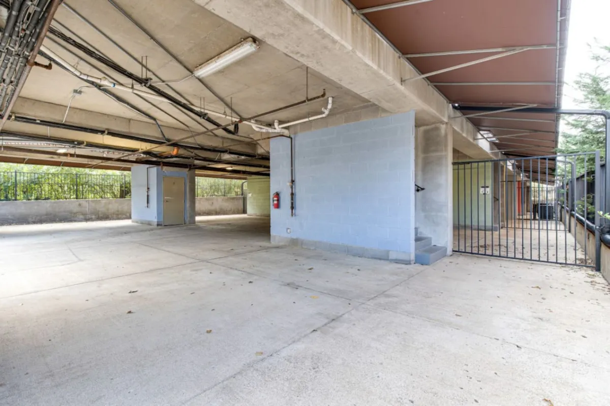 A functional and secure garage space with concrete flooring, robust metal railings, a security gate, and exposed pipes. The area is designed for both vehicle and bicycle storage, ensuring residents have ample and protected parking.