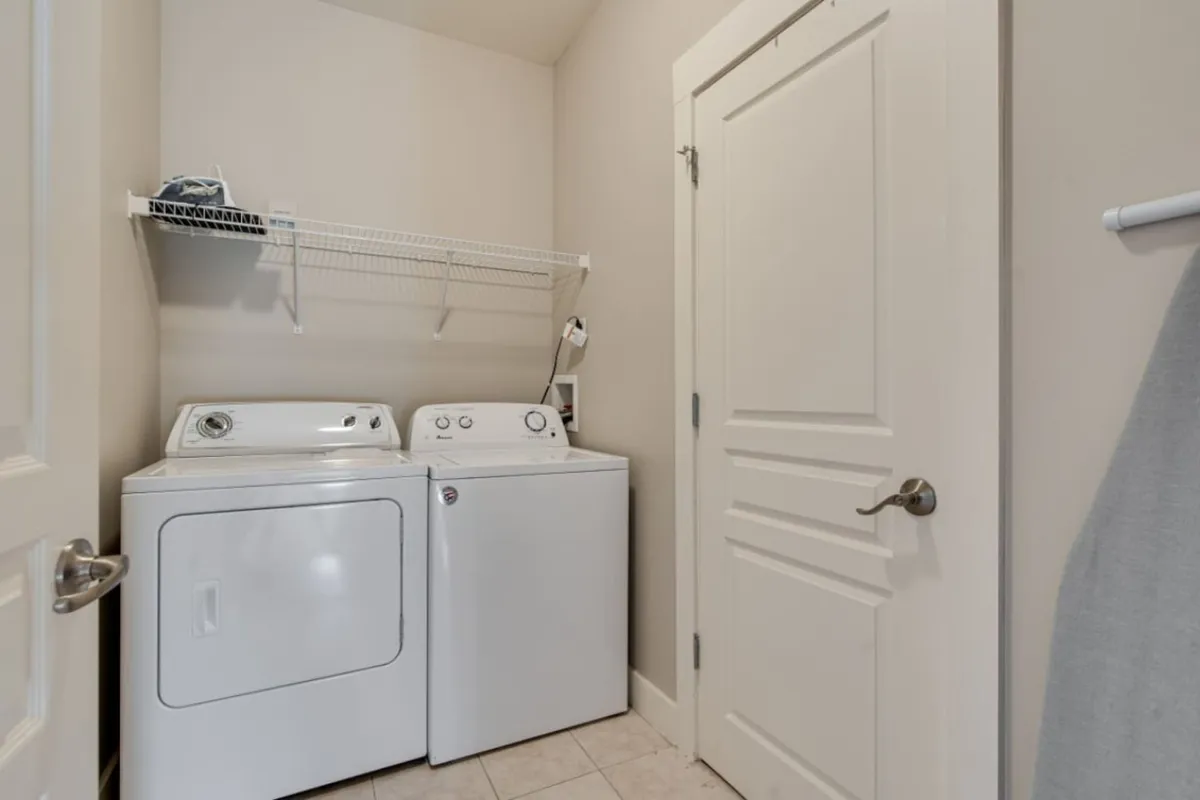 A practical laundry area with a washing machine, dryer, and a shelf for organizing cleaning supplies. The space is tidy and efficient, signaling the convenience of in-unit laundry for guests who prefer to pack light or need to freshen up during their stay.