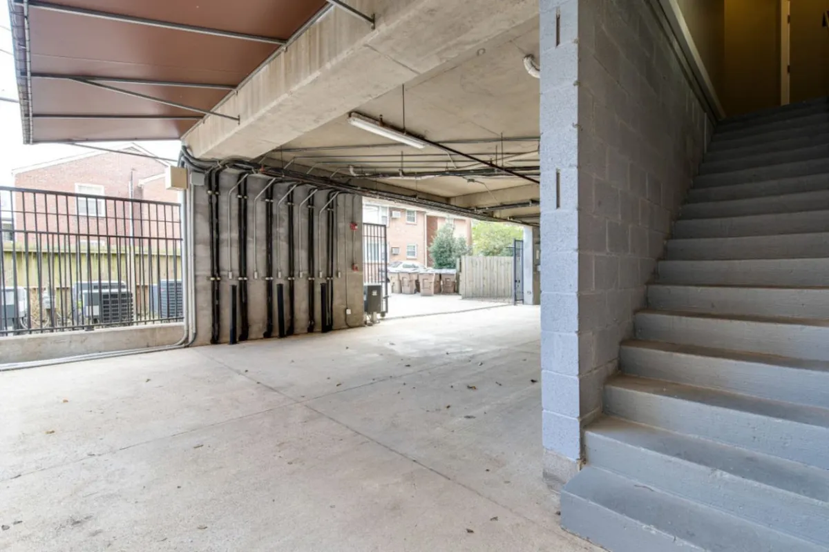 This image captures a practical, well-lit garage area featuring a staircase leading up to the living spaces, a visible security gate, and plenty of open space for vehicle parking and bicycle storage. The clean lines and organized layout emphasize ease of access and security for residents.