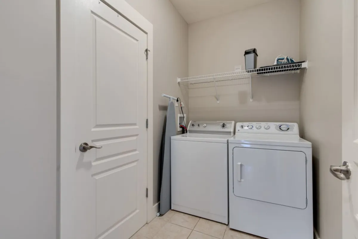 This scene presents a designated laundry area with a washing machine, dryer, and ironing board, showcasing the super-condo's practical amenities for longer stays. The space is organized and clearly designed for guest use.